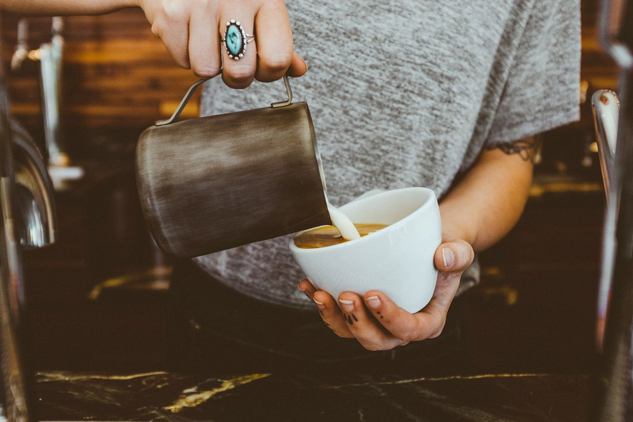 pouring milk into coffee in white cup